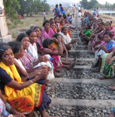 Women sit on the tracks, with the factory behind.
